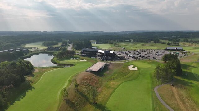 Aerial shot of TPC Toronto at Osprey Valley, showing fairways, greens, bunkers, clubhouse, parking area and reflective ponds under soft sun rays breaking through the clouds.