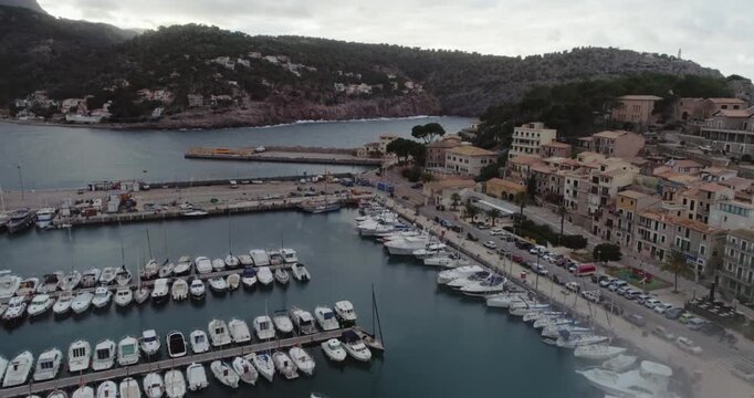 High-angle aerial view of a picturesque Mediterranean harbor (Port de Soller, Mallorca), showcasing a curved bay filled with a dense marina of docked yachts and boats, traditional seaside town