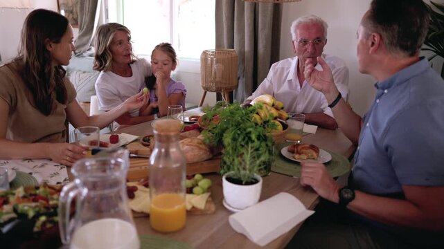 Happy multi generational family enjoying a meal together at a beautifully set dining table. Grandparents, parents, and a child are talking, eating, and sharing a moment of connection at home