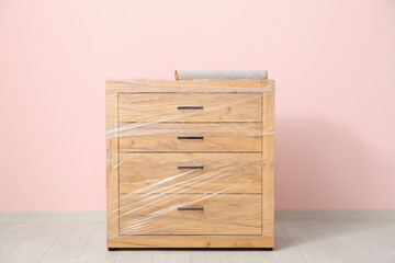 Wrapped chest of drawers with stretch film near pink wall in room on moving day