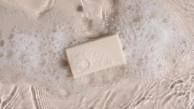 A bar of soap on a water surface with bubbles of white soapy foam. Concept of bath products, skin care products advertisement spa cosmetics. Body care and relaxation. High quality 4k footage