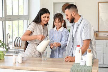 Happy parents with their little daughter pouring milk in kitchen