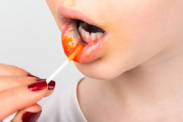 Close-up of hand applying bright orange lipstick to lips, isolated on white background, showcasing beauty and makeup detail.