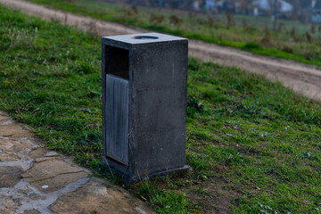 Square concrete trash bin placed on a grassy area near a path, ideal for modern parks and urban outdoor settings.