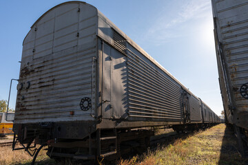 Long row of weathered freight train cars in sunlight, showcasing metal textures and industrial design, suitable for transport, travel, or industry themes.