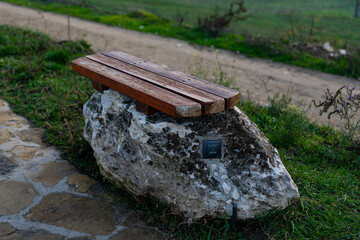 Outdoor wooden bench set on a large rock with electrical outlet, surrounded by grass and pathway in a natural park setting.
