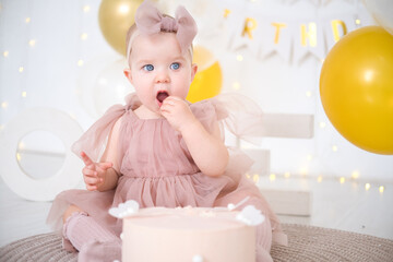 little beautiful blue-eyed girl celebrates her first birthday and tastes her first birthday cake