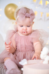 little beautiful blue-eyed girl celebrates her first birthday and tastes her first birthday cake