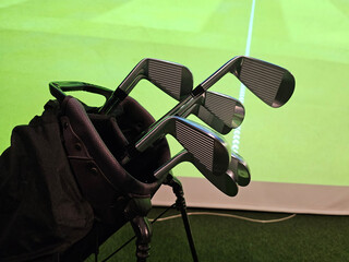 Golf clubs lean against a bag on the ground with a green screen behind
