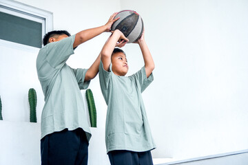 Older Asian Boy Teaching Younger Boy How To Play Basketball