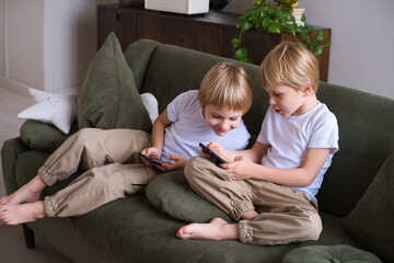 kids blonde boys twins using smartphones on the couch in living room