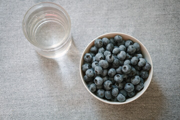 Plate full of fresh ripe blueberry and glass of water, flatlay. Lots of sweet berries as healthy dessert. Summer fruits on the table. Natural source of vitamins, healthy eating