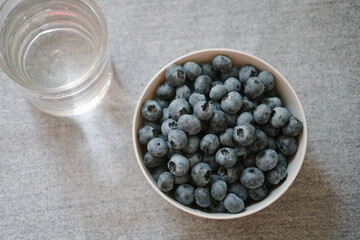 Plate full of fresh ripe blueberry and glass of water, view from above. Sweet small berries as healthy dessert. Summer fruits on the table. Natural source of vitamins