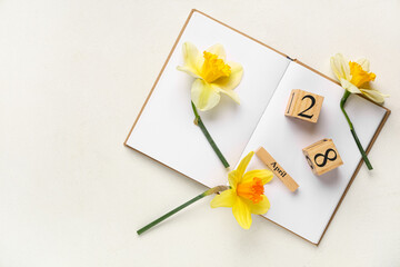 Cube calendar with date 28 April, open book and beautiful narcissus flowers on light background