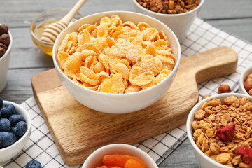 Bowls with cornflakes and ingredients on grey wooden background, closeup