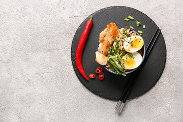 Bowl of ramen noodle soup with chicken and cucumber slices on white background