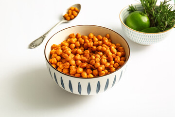 Bowl of tasty fried chickpeas with lime and rosemary on white background