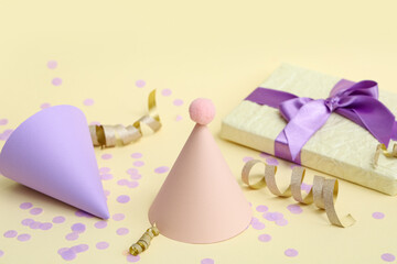 Party hats with gift box and confetti on yellow background