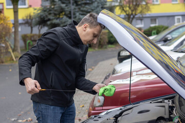 A man inspects lubricant quality using an oil dipstick in a parking area