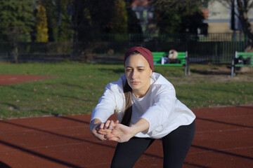 A woman performs squats as part of her warm-up routine in a grassy area near a track