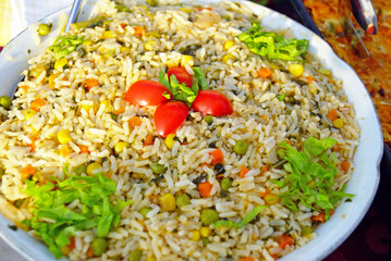 Colorful vegetable rice pilaf with corn, peas, and carrots, topped with cherry tomatoes and herbs. Symbolizes healthy side dish options, plant-forward catering, vegan diet, and balanced meal planning.