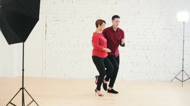 Loving family couple in red shirts - female and male is dancing together in studio