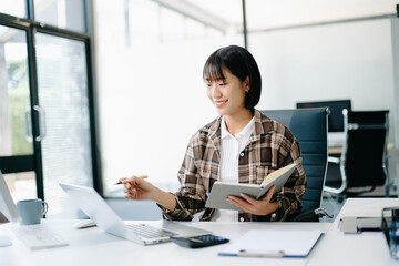 Confident Asian woman with a smile standing holding notepad and tablet at the modern office.