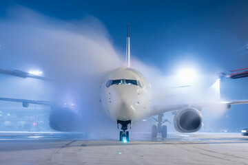 De-icing an airplane shortly before take off. Freezing winter night at snowy airport.