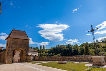 View of an old village gate, a metal cross, and traditional architecture under blue sky