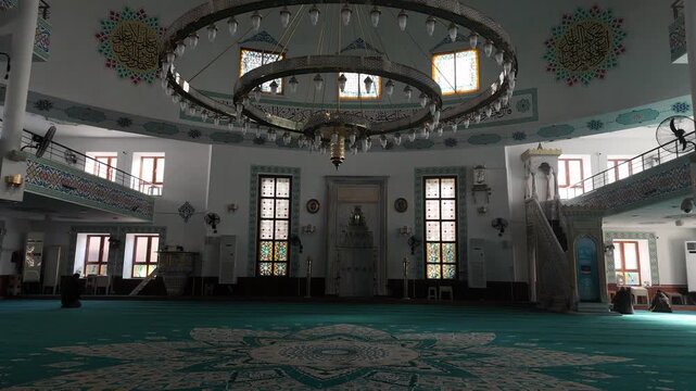 Interior footage of a mosque featuring a wooden minbar, prayer hall, and richly decorated carpets with traditional Turkish patterns. The scene reflects Islamic architecture, spirituality, and the art