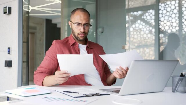 Frustrated businessman unhappy with bad financial results while checking report documents while sitting at a workplace in a business office. Confused puzzled employee having difficulty with paperwork