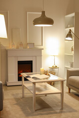 Obraz premium Interior of elegant living room with fireplace, glass coffee table and glowing lamps at evening