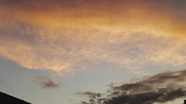 golden shelf cloud at sunset horizon, dramatic orange underside and layered dark clouds, rooftop silhouette