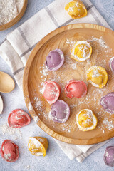 Wooden plate with colorful raw dumplings and flour on white background
