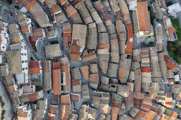 Aerial view of a medieval town unfolds with terracotta rooftops cascading down gentle slopes, a tapestry of earthy hues against the backdrop of winding streets, Rocca Imperiale, Calabria, Italy.