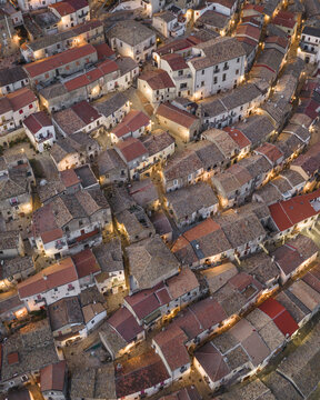 Aerial view of a sun-kissed tapestry of terracotta rooftops and winding alleys, where the warm glow of lights paints a tranquil village scene, Rocca Imperiale, Calabria, Italy.