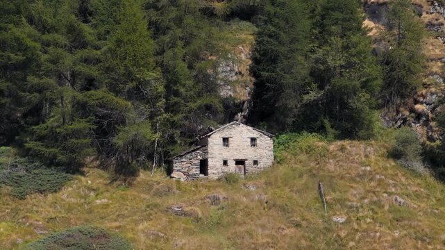Close-up orbiting right aerial view of a mountain house in Valtournenche, Aosta Valley, Valle d&rsquo;Aosta, surrounded by dense pine forest