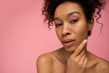 Young woman with stylish makeup posing against a vibrant pink background