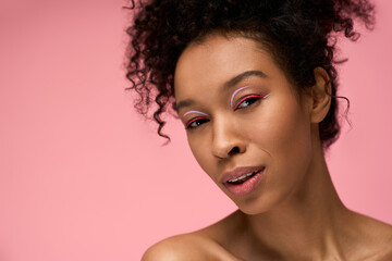 Beautiful young woman with curly hair and vibrant makeup against a pink background