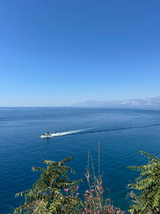 Aerial view of the vast deep blue sea, captured from above, with a small boat creating a subtle wake across the calm waters under a pristine clear sky