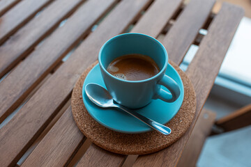 Close-up top view of cup of coffee, of cyan color on wooden table.