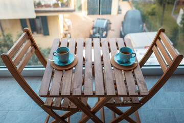 Two cups of coffee of cyan color on wooden table with two chairs.