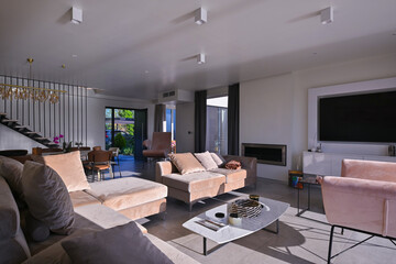 Obraz premium Modern luxury living room interior at sunset. Open-plan space featuring beige sofas, marble dining table, large glass windows with sun flare, and view of a patio. Stylish contemporary home design