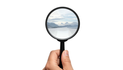 Hand holding magnifying glass revealing distant mountainous landscape