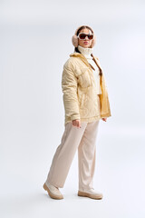 Fototapeta premium Trendy teenage girl showcases winter fashion in a chic white studio setting