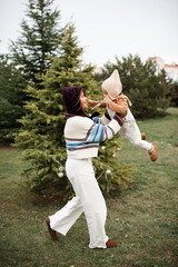 Young woman holding baby girl 1-2 year old decorating Christmas tree outdoors over nature background. Winter holiday season. Motherhood.