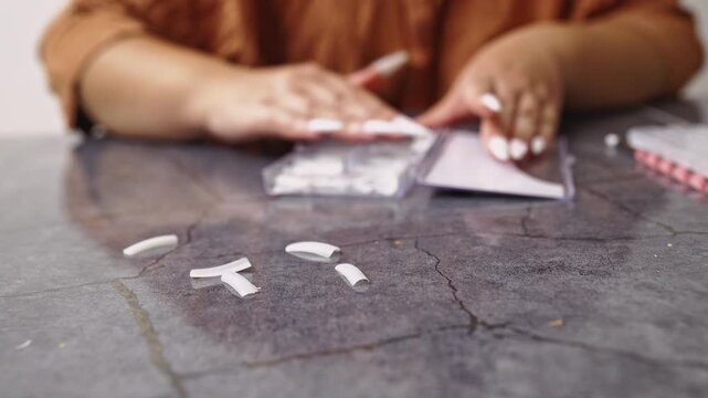 A close-up view of a woman's hands as she meticulously removes her long white artificial nails. Capturing a common beauty routine and the process of self-care and nail maintenance.