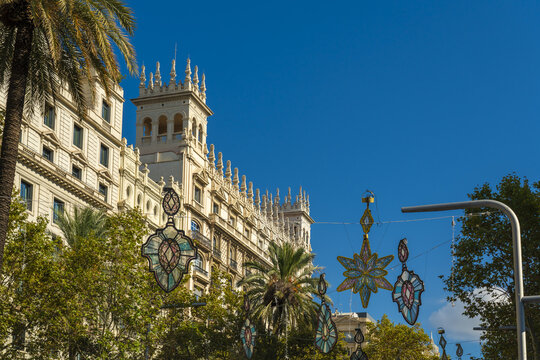 View of ornate earrings dangle beneath the clear blue sky, casting shadows on the trees and the elegant building, Barcelona, Catalonia, Spain.