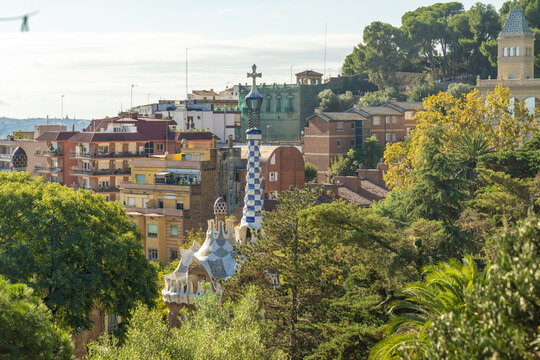 View of whimsical architecture rising amidst lush greenery under a bright sky, with colorful buildings dotting the landscape, Barcelona, Catalonia, Spain.