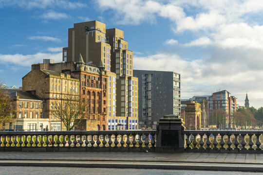 View of a skyline where old brick buildings meet modern architecture under a bright, partially cloudy sky, creating a vibrant contrast of eras, Glasgow, Scotland, United Kingdom.